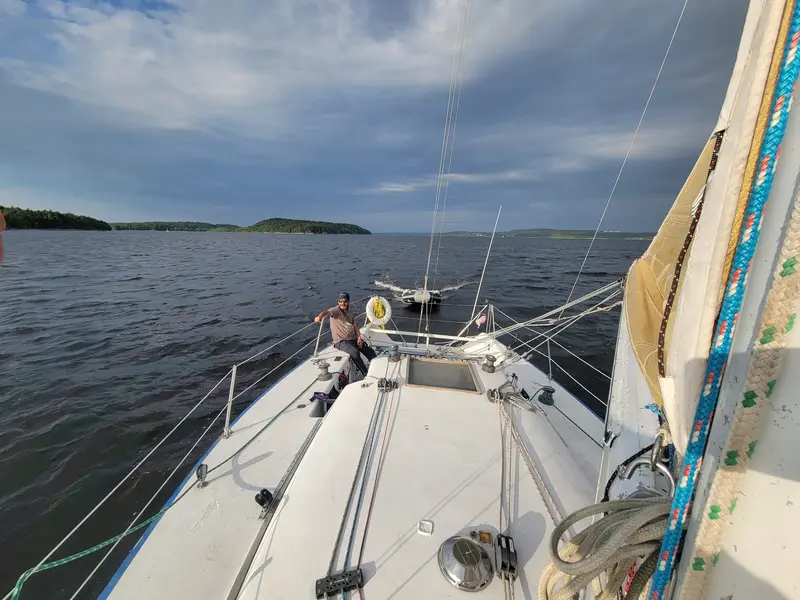Looking forward along a white foredeck toward the wide Saint John River under a cloudy sky