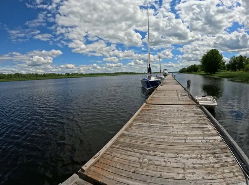 A long wooden dock running out into calm water under summer clouds