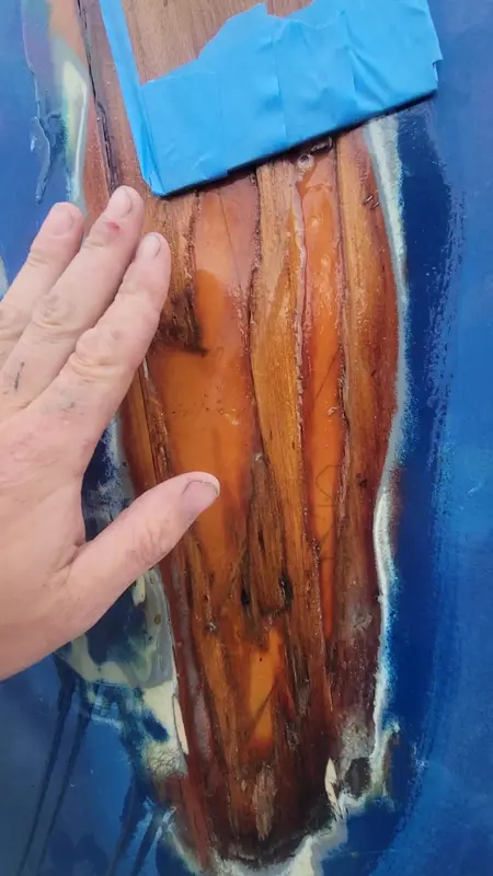 A hand resting beside bare timber exposed in a blue painted hull during a plank repair