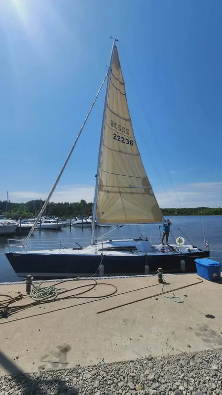 The same sloop at a marina dock with her headsail hoisted against a blue sky